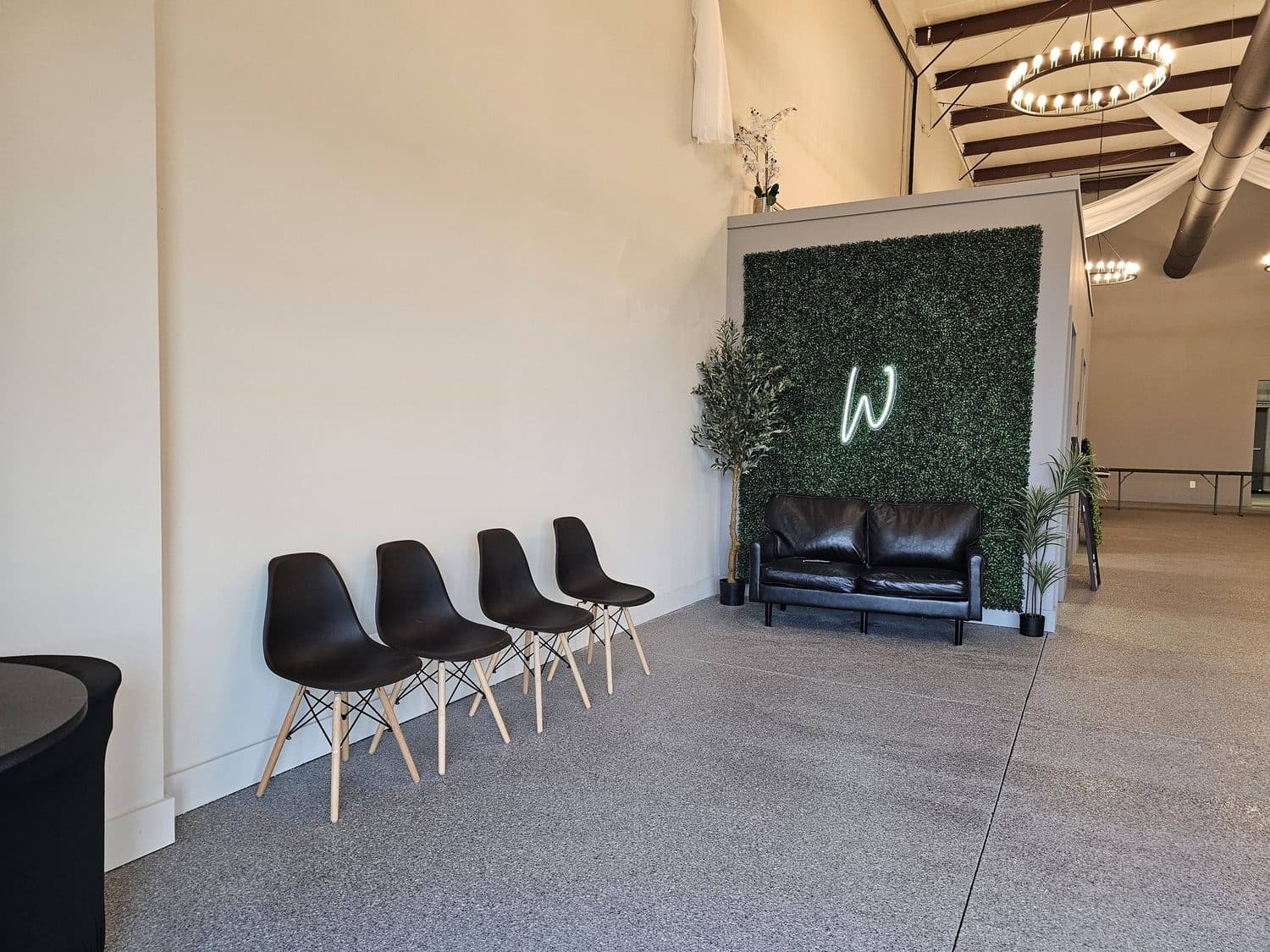 Black molded chairs in a row beside a leather loveseat, facing a boxwood wall with a white W monogram
