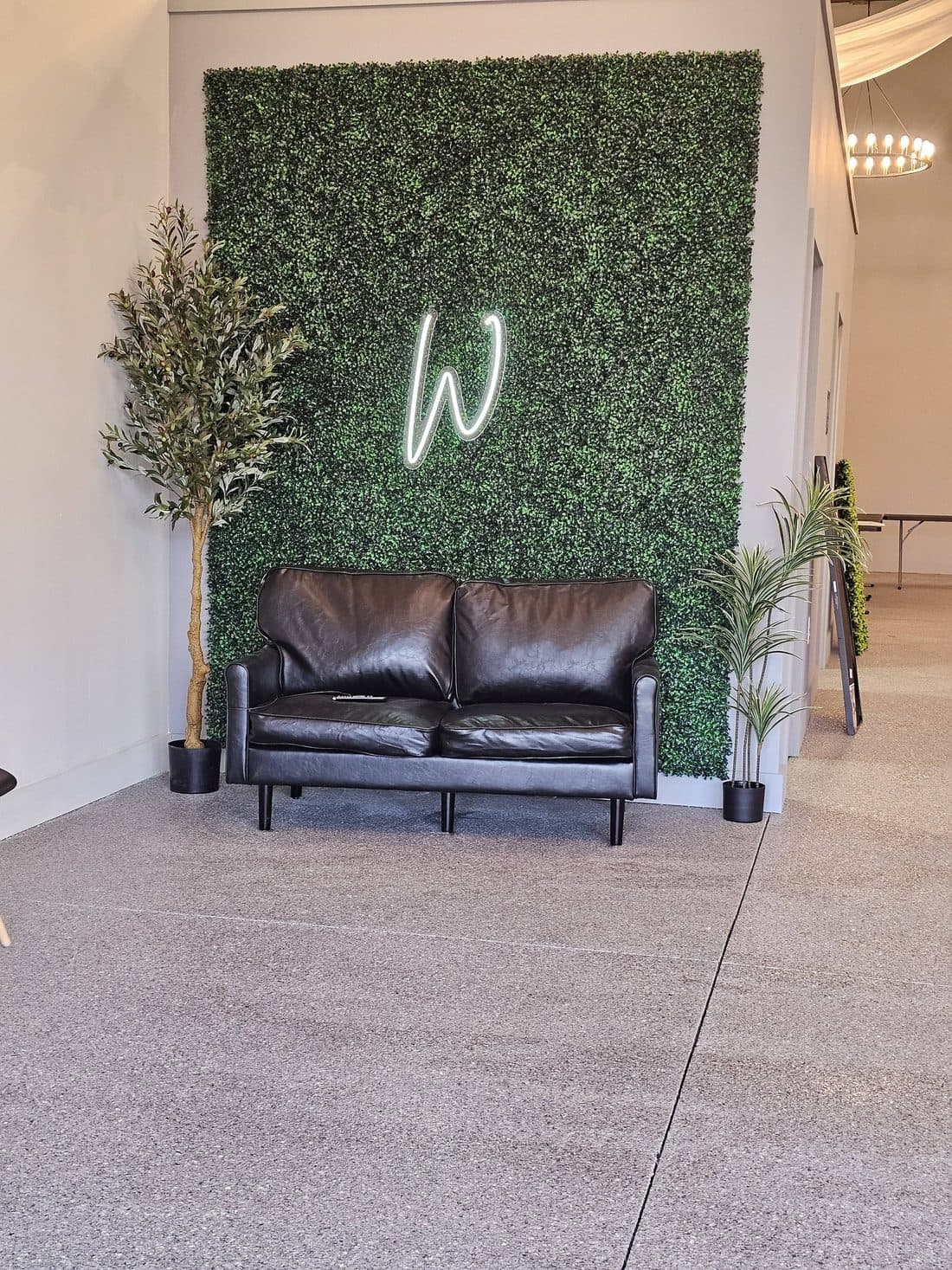 The boxwood monogram wall at Willow Tree Events, with a leather loveseat in front of it and a ring pendant overhead